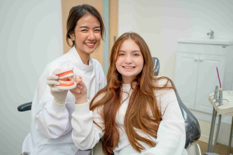 Smiling dentist and young patient holding a dental model.